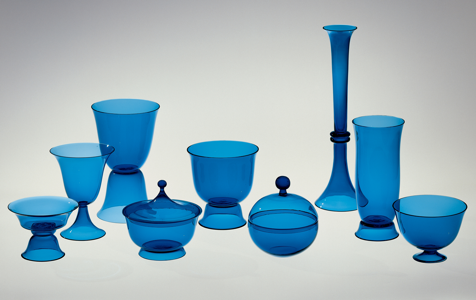 Tableware Set of Nine Blown Vessels, 1916. Designed by Josef Hoffmann (Austrian, 1870–1956); manufactured by Wiener Werkstätte and probably Meyr’s Neffe. Mold-blown and hot-worked glass. Smallest object: H. 8.2 cm, Diam. 11.6 cm; Tallest object: H. 32.8 cm, Diam. 9.5 cm. The Corning Museum of Glass (74.3.24).
