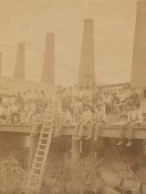 old sepia photo of outside of glassworks, with workers