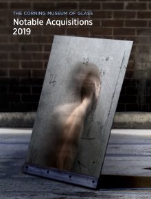The front cover of a book with the title "Notable Acquisitions 2019" in white bold letters at the top, and a photograph of a metallic, reflective rectangular with numbers searched on the surface and a person facing away