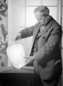 Photograph of René Lalique looking at a colorless version of the Lézards et bleuets (Lizards and bluets) vase, designed in 1913. The photo was taken around 1925. The Corning Museum of Glass has an opaque black version of this vase.